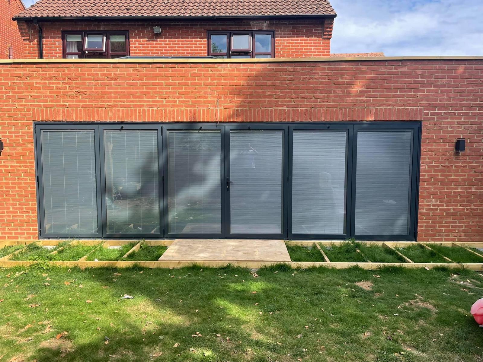 Six leaf anthracite grey aluminium bi-fold doors with integral blinds on a red brick extension in Peterborough