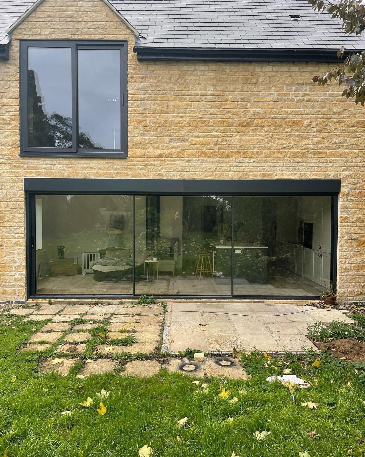 Large anthracite grey aluminium sliding patio doors in a natural stone house elevation in Rutland
