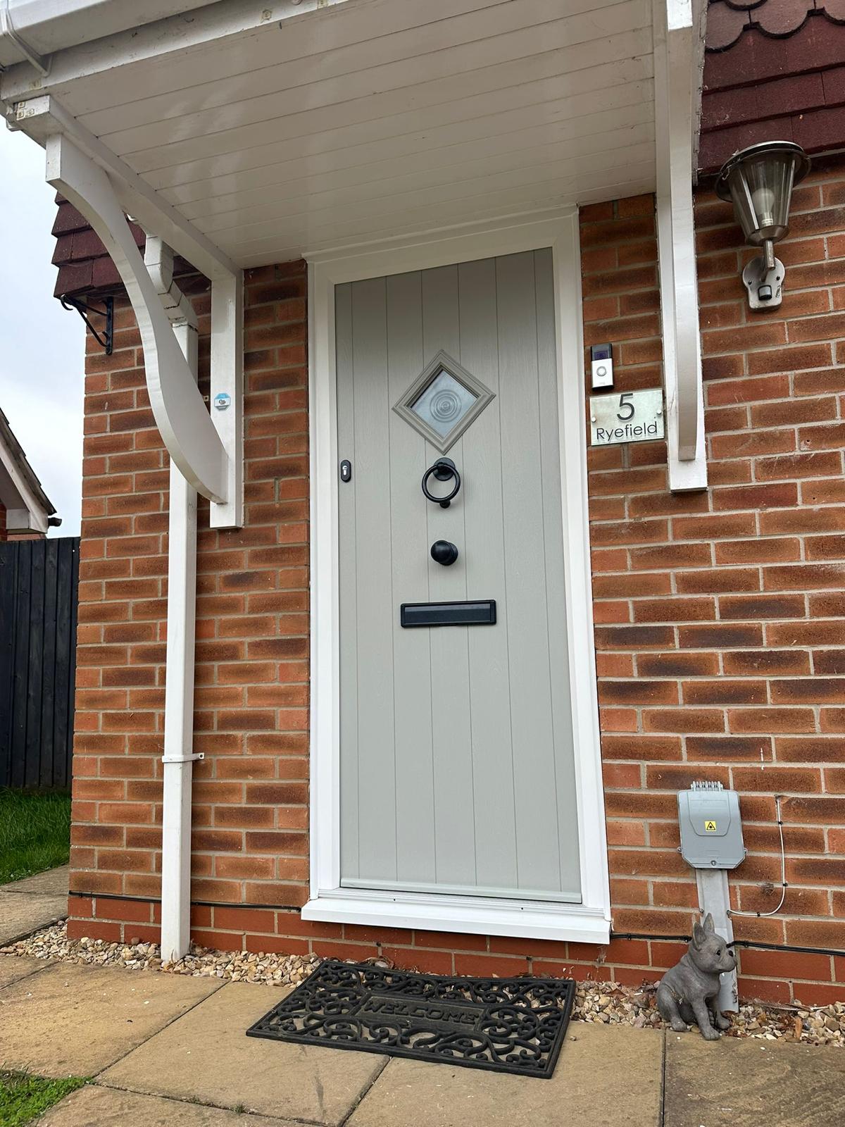 Pebble grey composite front door with a diamond bullseye light and black ironmongery under a canopy porch in Lincolnshire