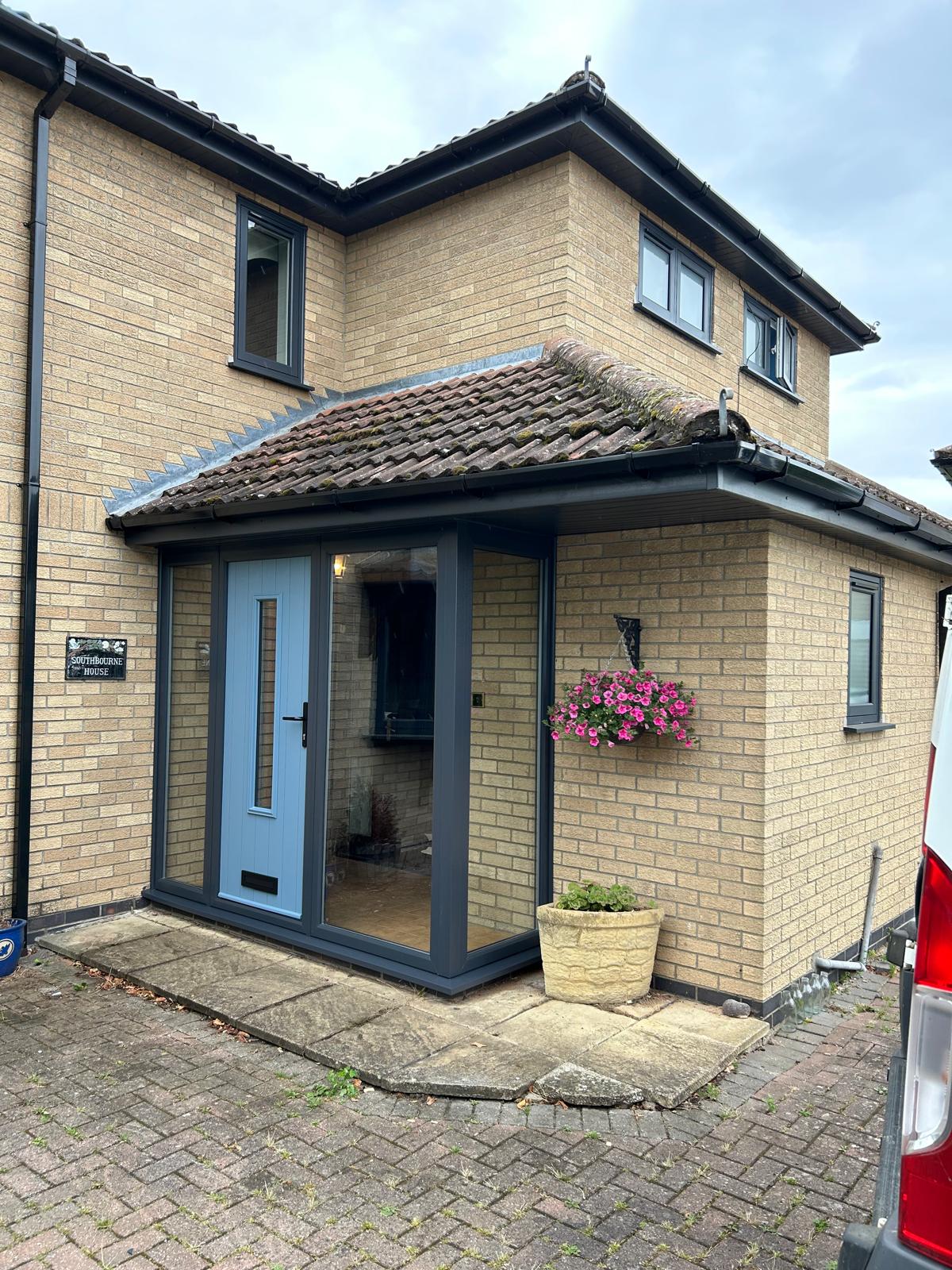 Anthracite glazed porch enclosure with duck egg blue composite door built under a tiled canopy in Stamford