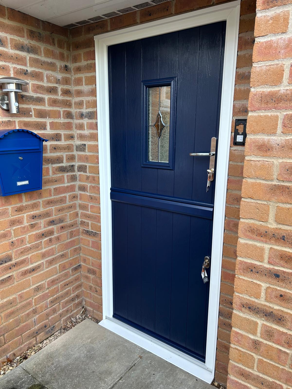 Navy blue composite stable door with leaded glazed panel and white frame on a brick house in Bourne