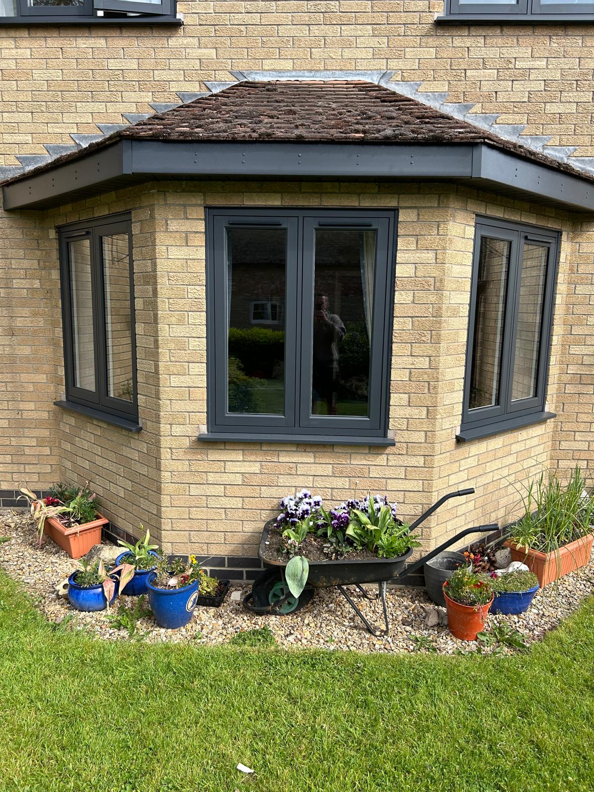 Anthracite grey UPVC splayed bay window beneath a retained tiled bay roof on a stone house in Stamford