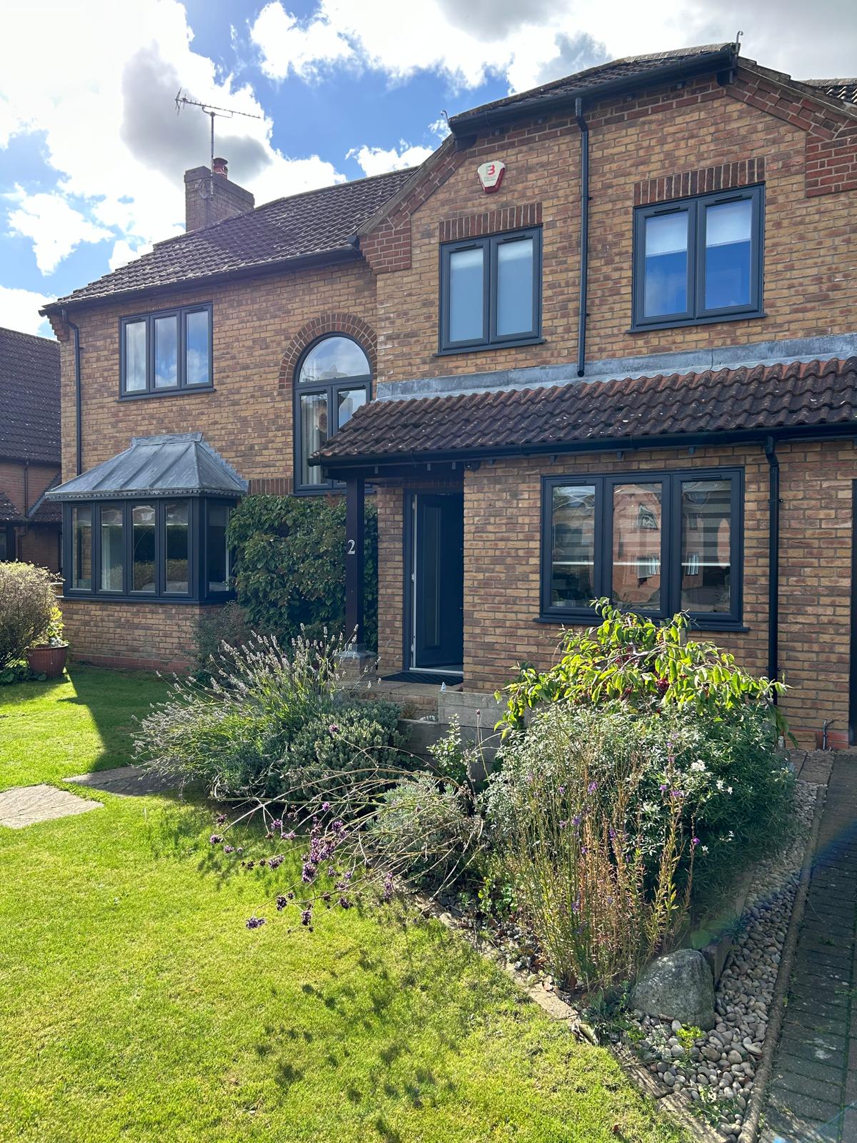 Detached brick house in Stamford with anthracite grey windows, arched stair window and matching conservatory frames