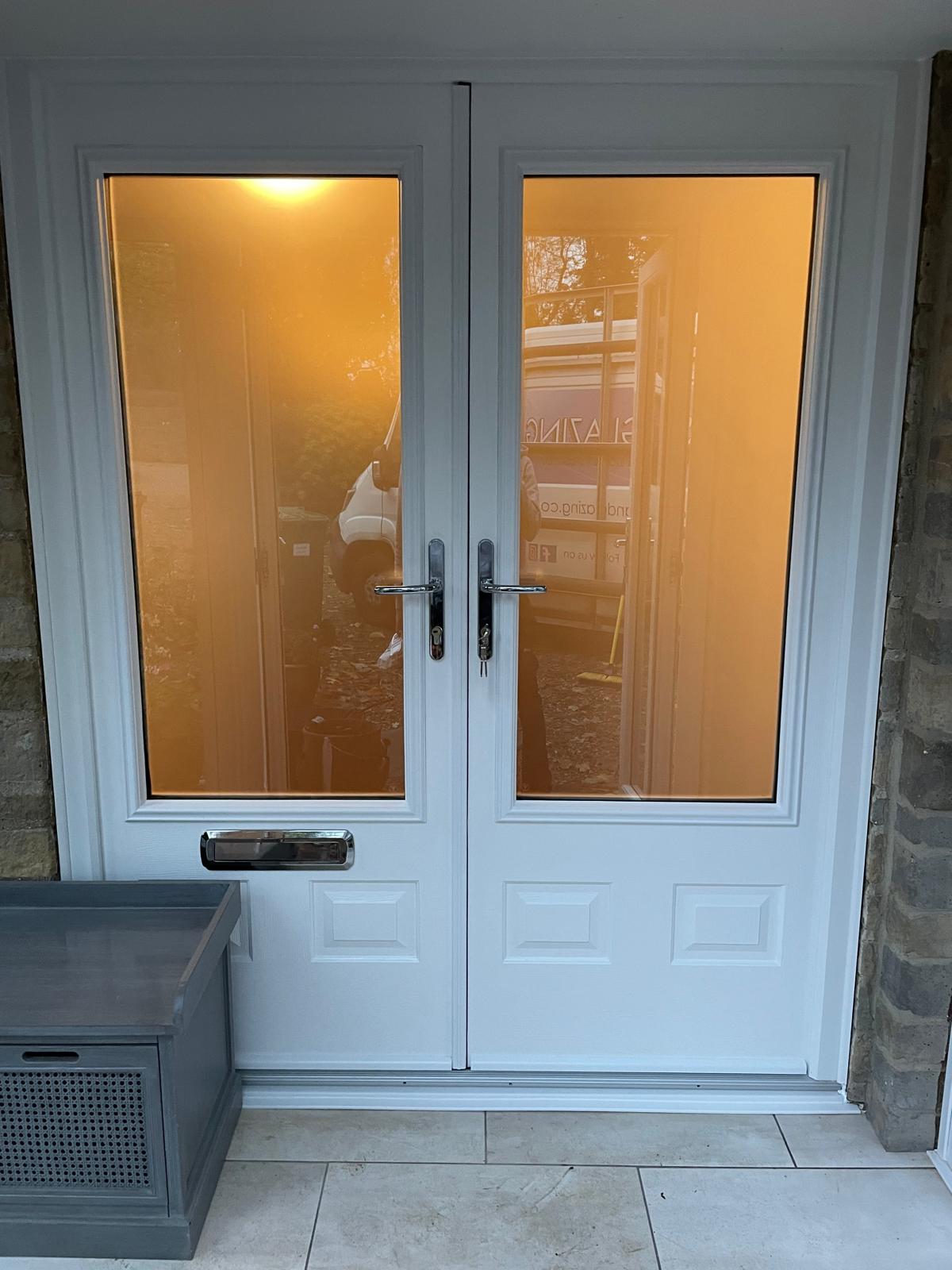 White panelled composite French doors with chrome handles and letterplate set in a stone opening in Rutland