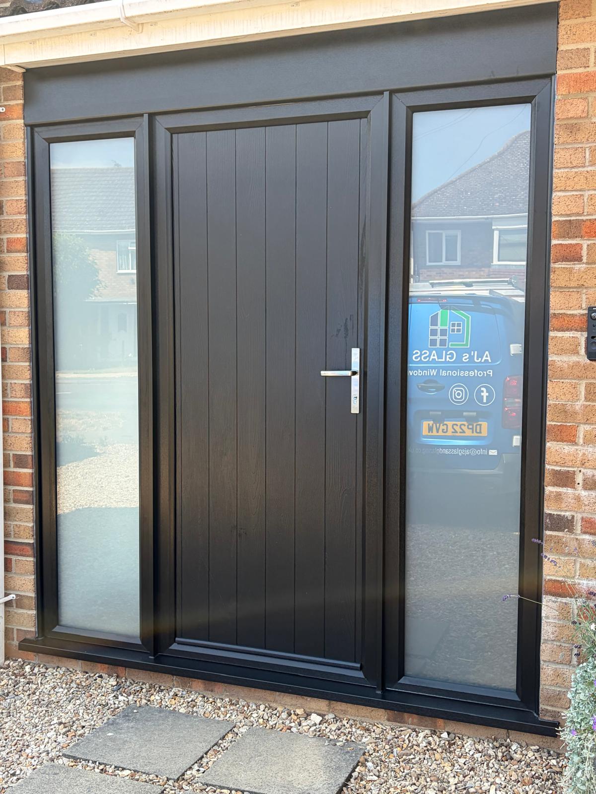 Black cottage-style composite front door with two obscure glazed side panels on a Bourne home
