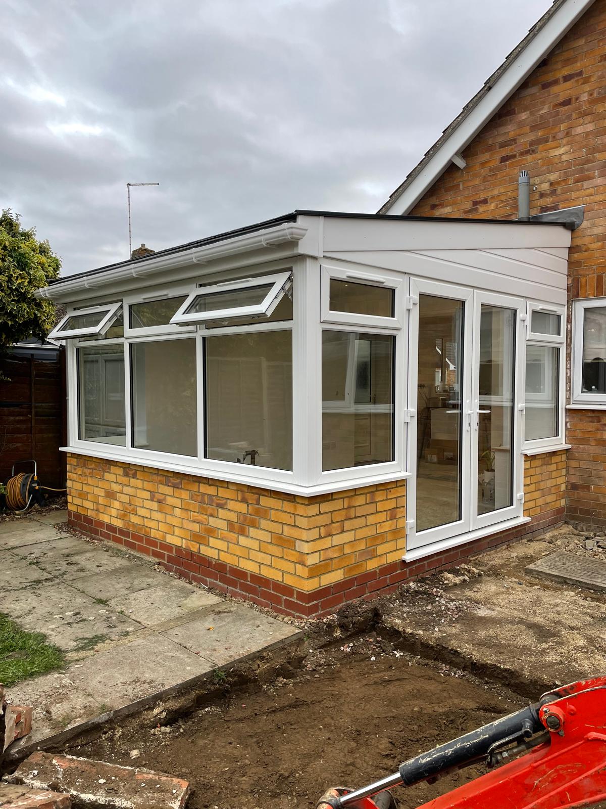 White UPVC conservatory with an insulated solid roof and French doors on a brick bungalow in Peterborough