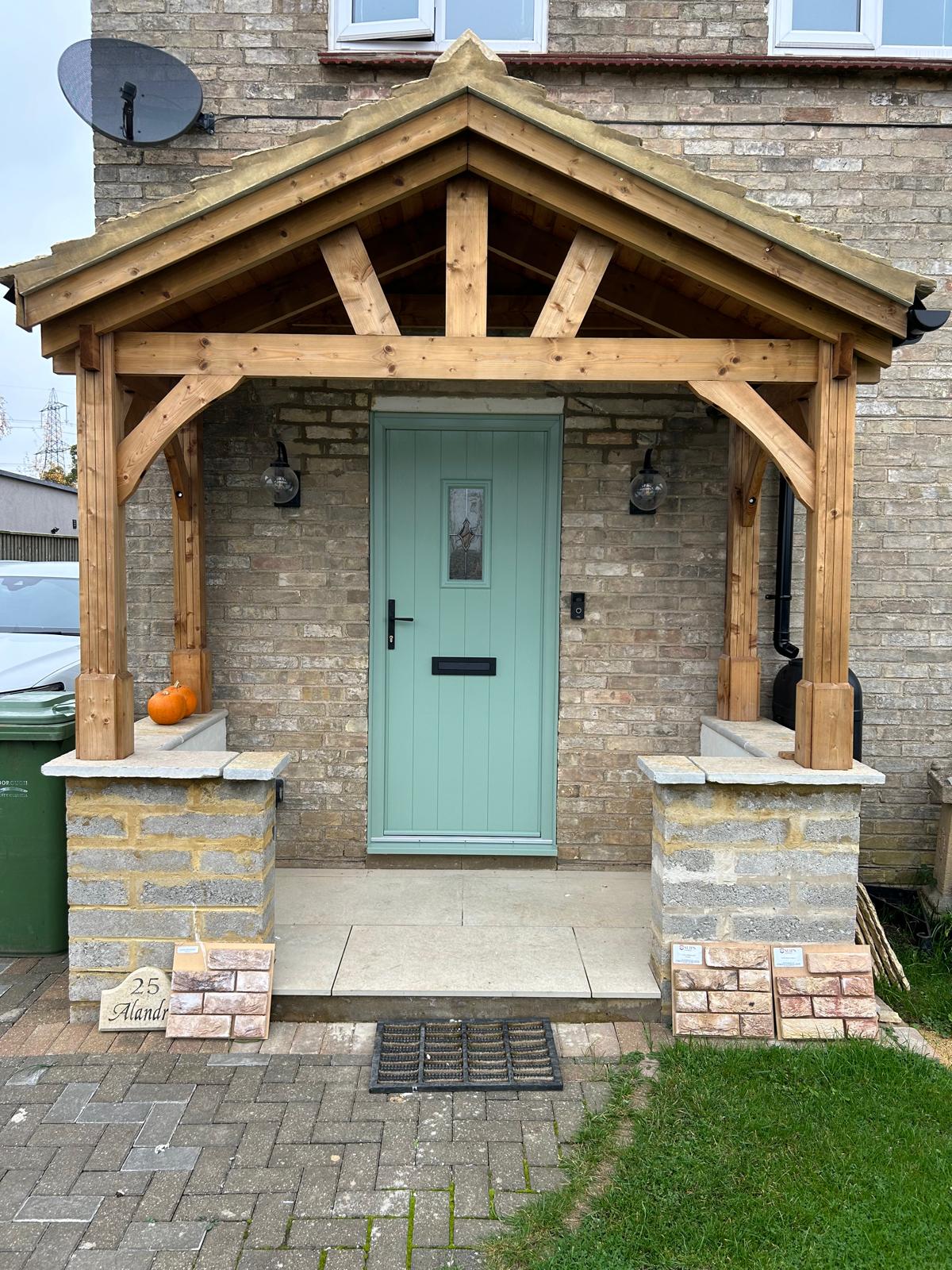 Sage green composite front door with leaded glass panel set beneath an oak framed porch in Bourne