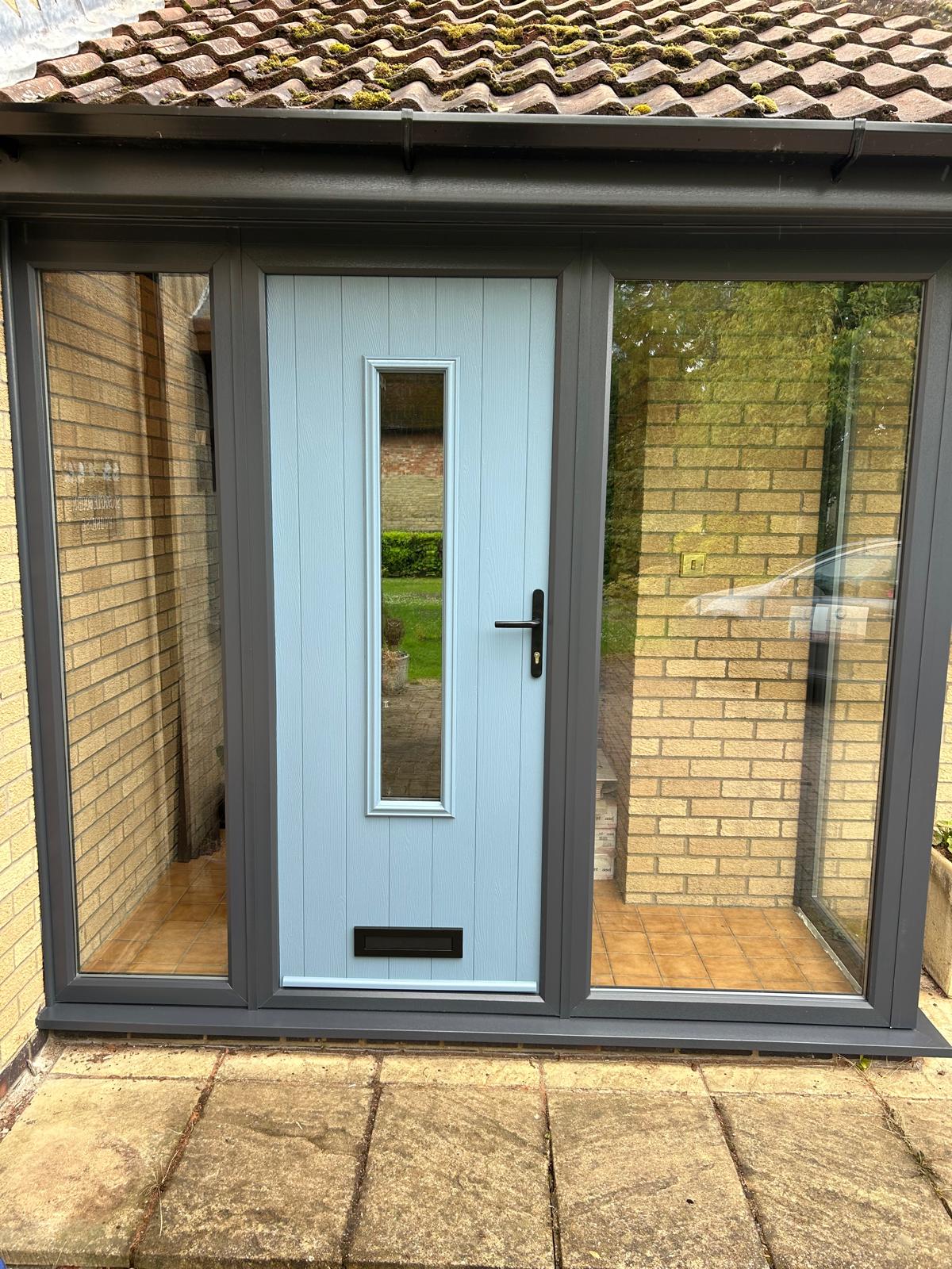 Front view of a glazed porch with duck egg blue composite door and full height anthracite framed side panels in Stamford