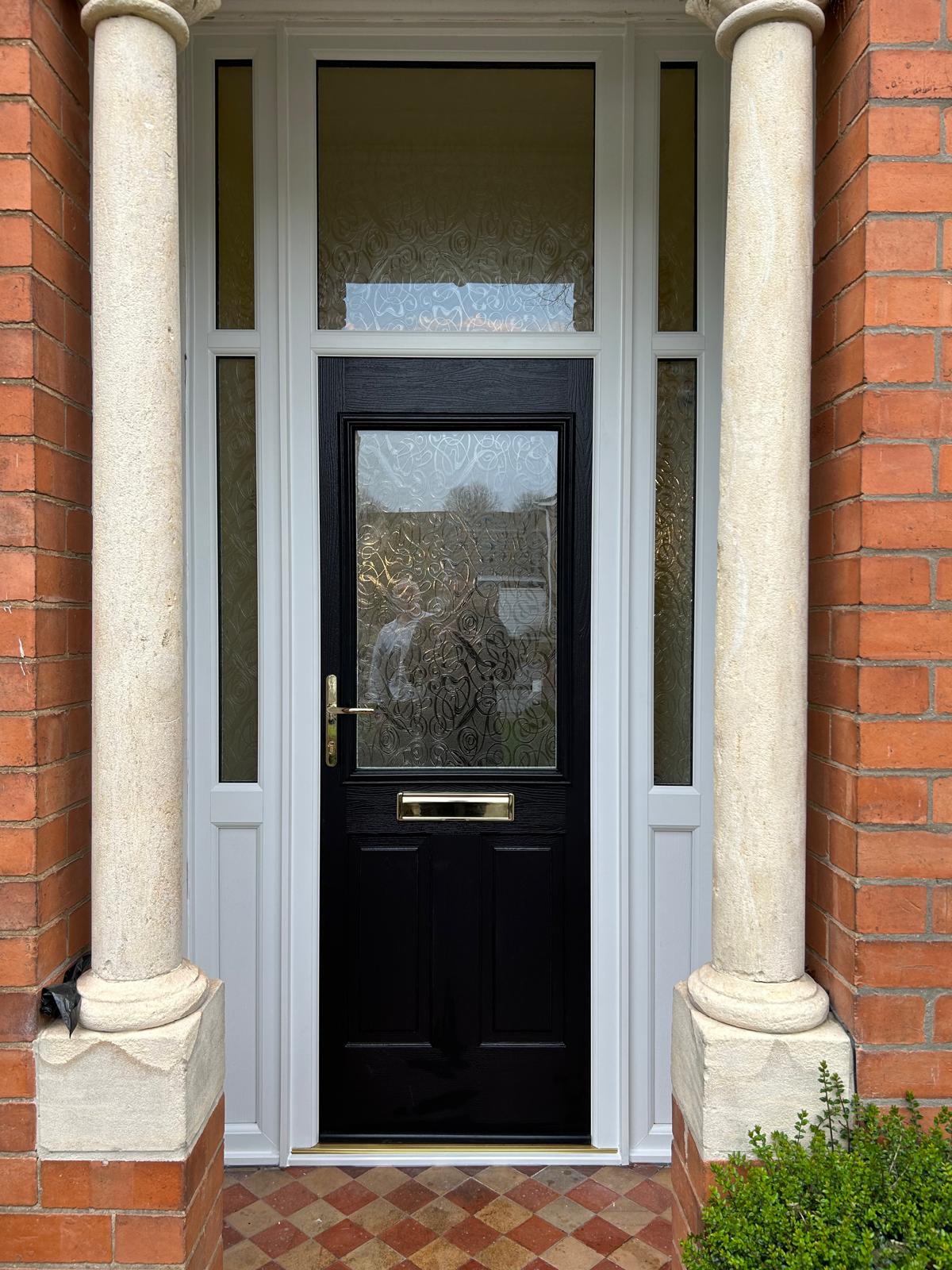 Black composite front door with brass letterplate, patterned glass, sidelights and fanlight in a Victorian stone columned porch in Stamford