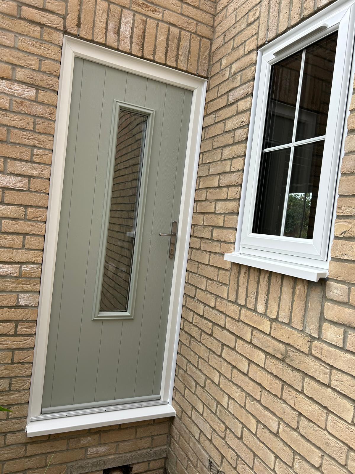 Chartwell green composite side door with a long glazed light next to a white casement window on a brick house in Bourne