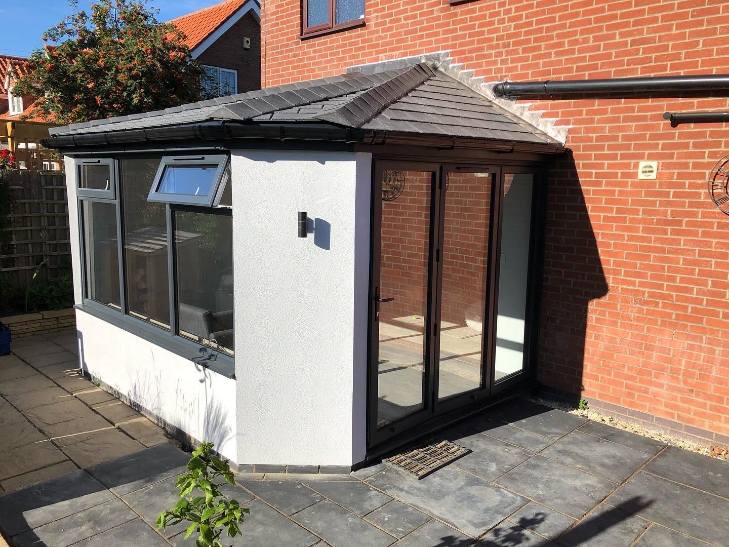 Rendered garden room with a tiled warm roof and black aluminium bi-fold doors installed in Bourne