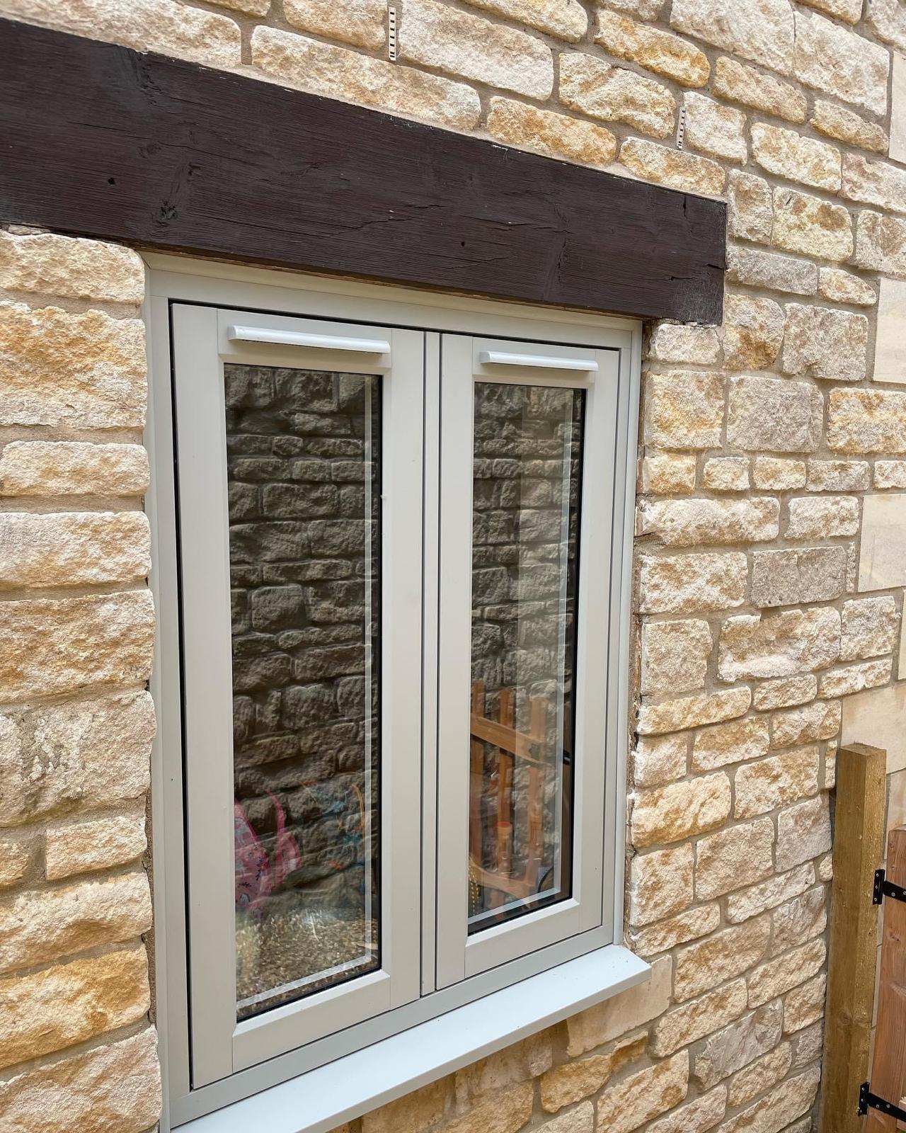 Agate grey flush casement window under a dark oak lintel in a Cotswold stone cottage wall in Rutland