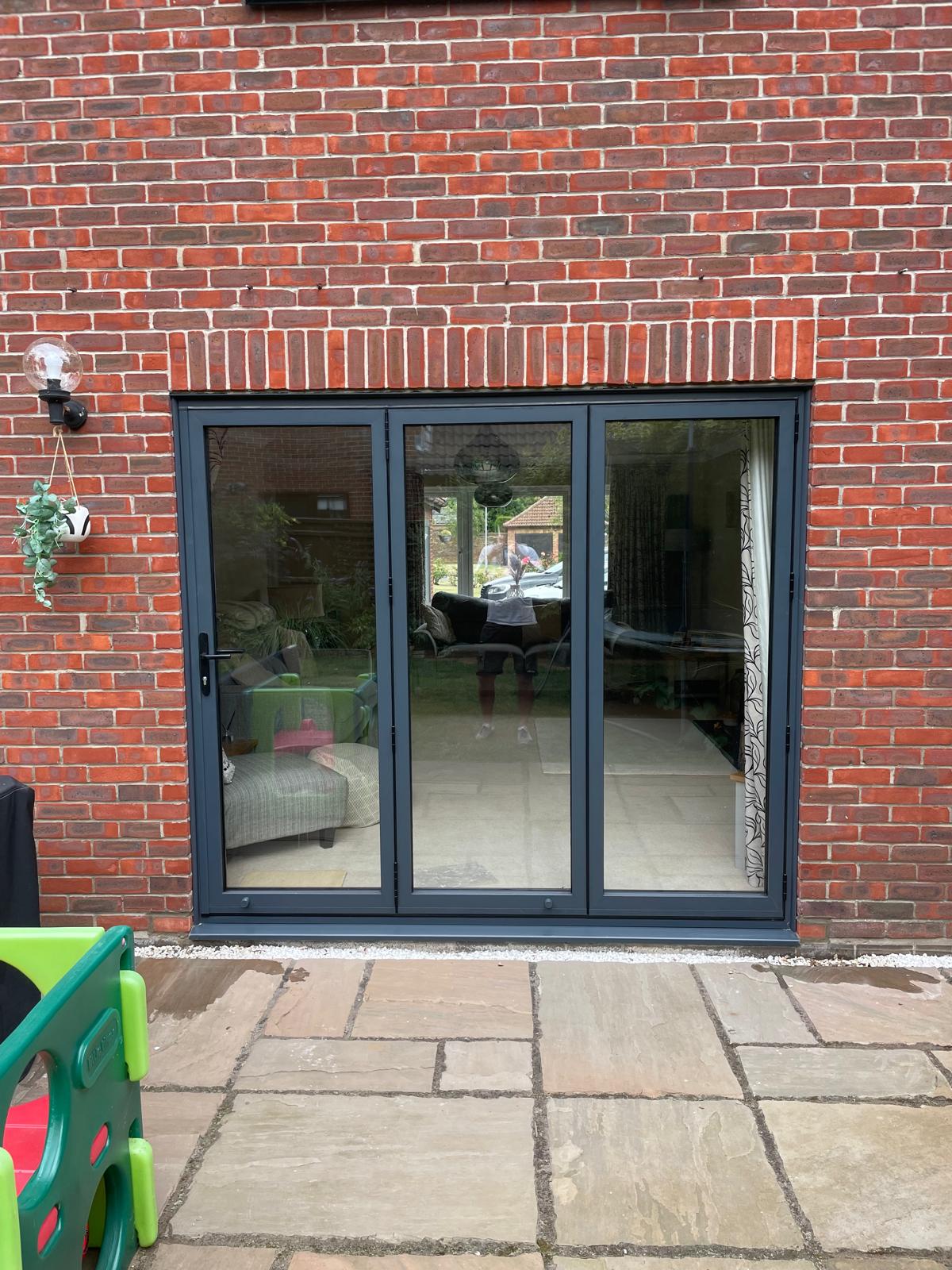 Anthracite grey three leaf aluminium bi-fold doors in a red brick wall opening onto a sandstone patio in Stamford