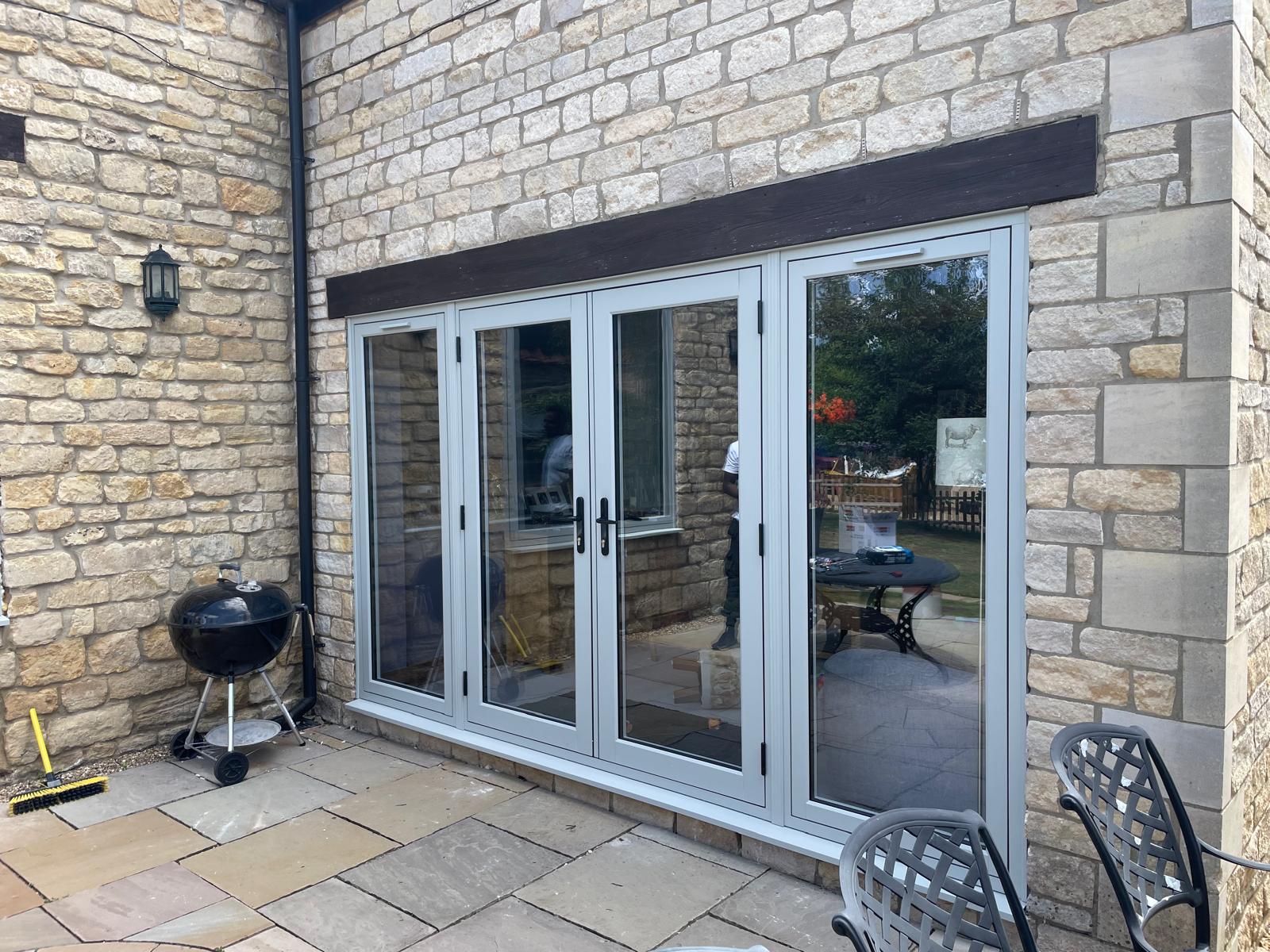 Agate grey four leaf UPVC bi-fold doors under an oak lintel in a limestone cottage wall opening onto a sandstone patio in Stamford