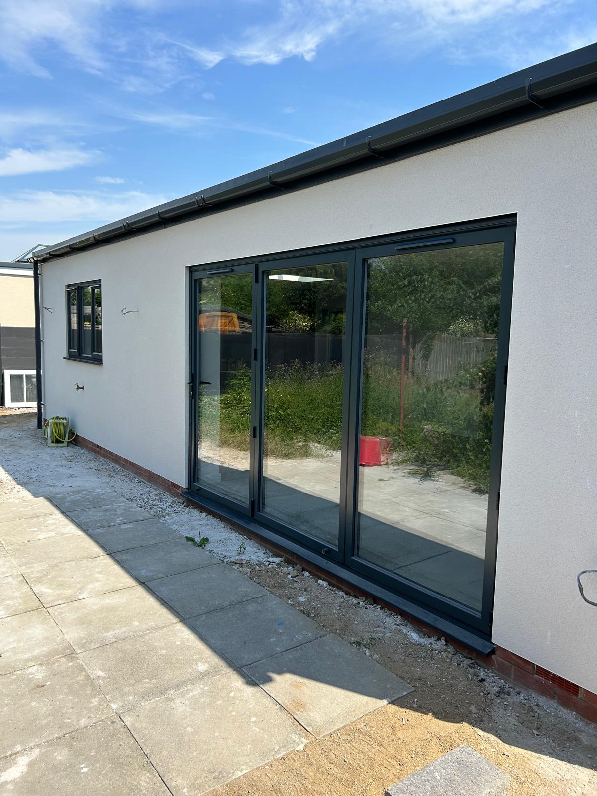 Anthracite grey three leaf aluminium bi-fold doors fitted to a rendered garden building in Lincolnshire