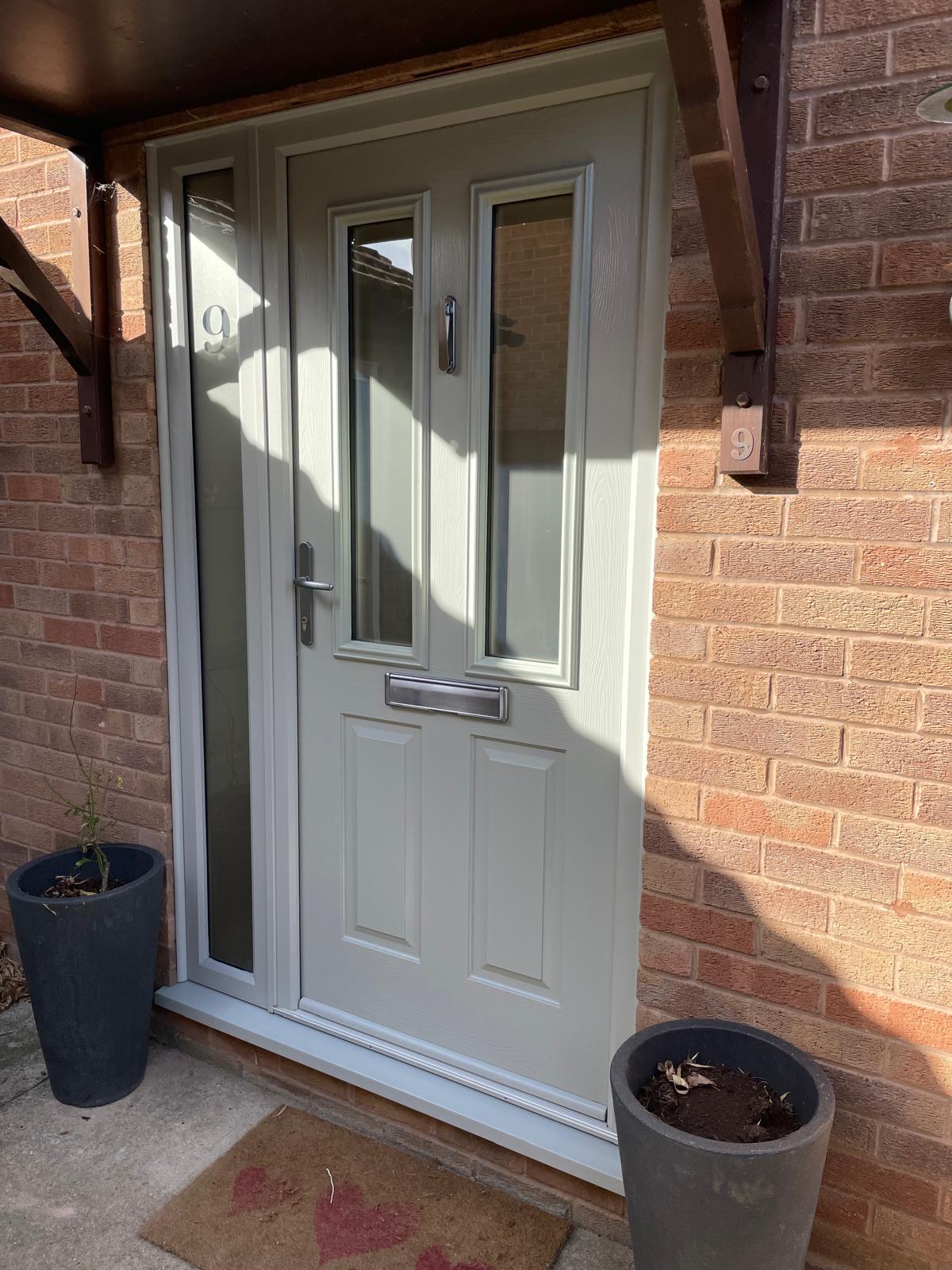 Pebble grey composite front door with twin glazed lights and an etched number sidelight under a timber canopy in Bourne